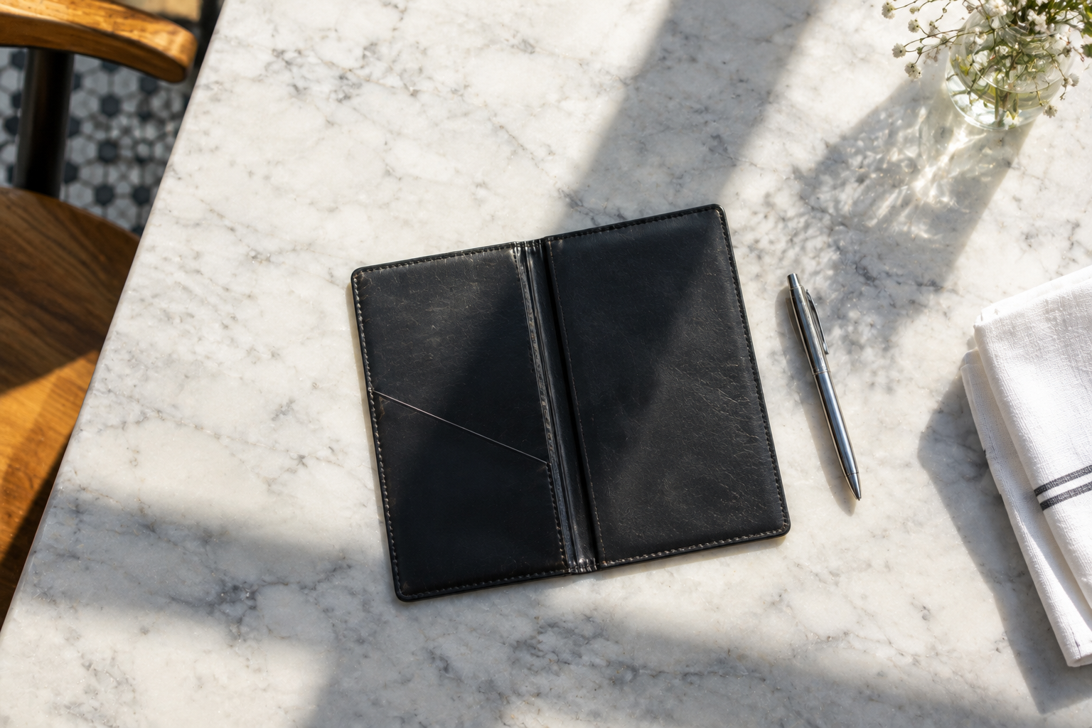 Open black check presenter and a pen on a sunlit marble bar top